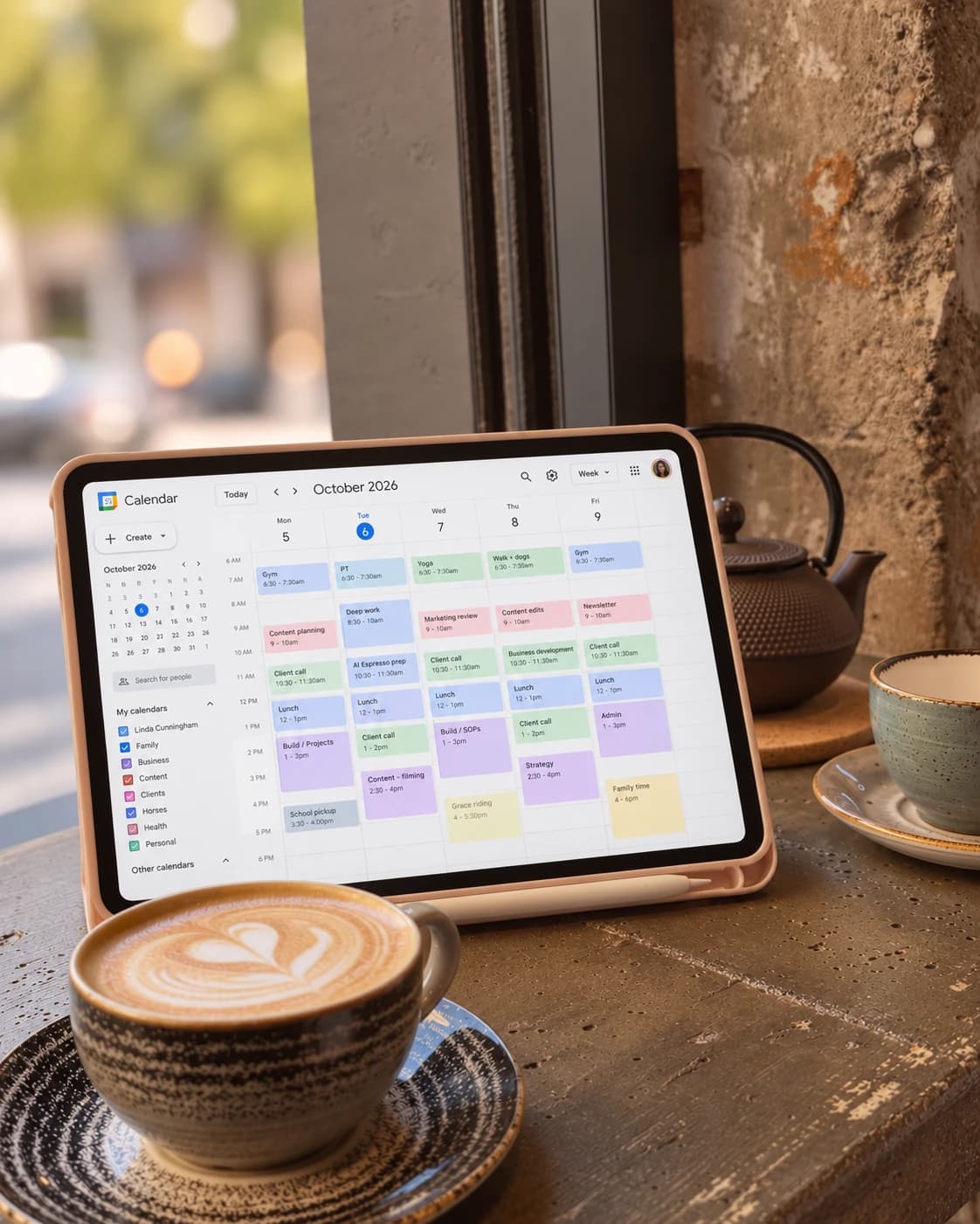A tablet showing a colour-coded weekly calendar beside a flat white on a café window ledge
